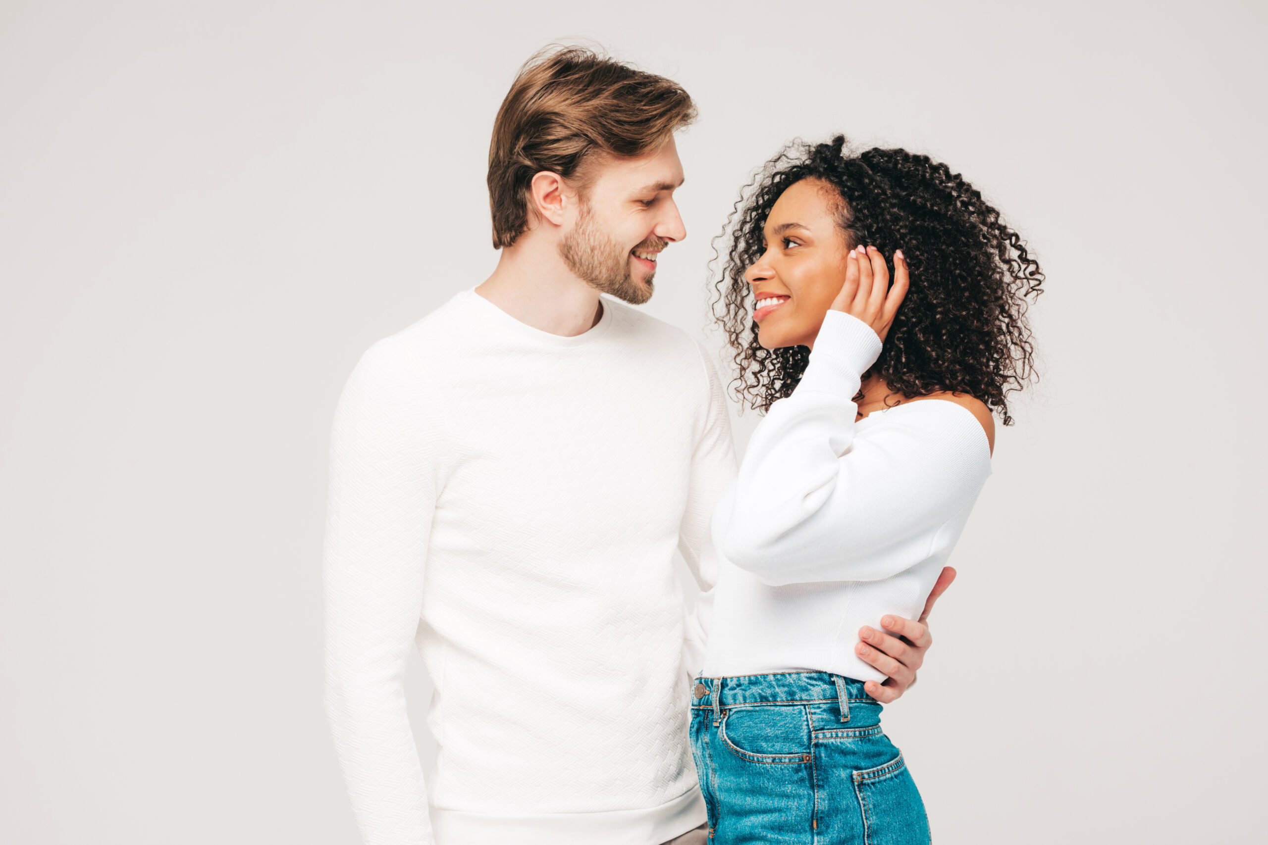 Smiling beautiful woman and her handsome boyfriend. Happy cheerful multiracial family having tender moments on grey background  in studio. Multiethnic models hugging. Embracing each other.Love concept